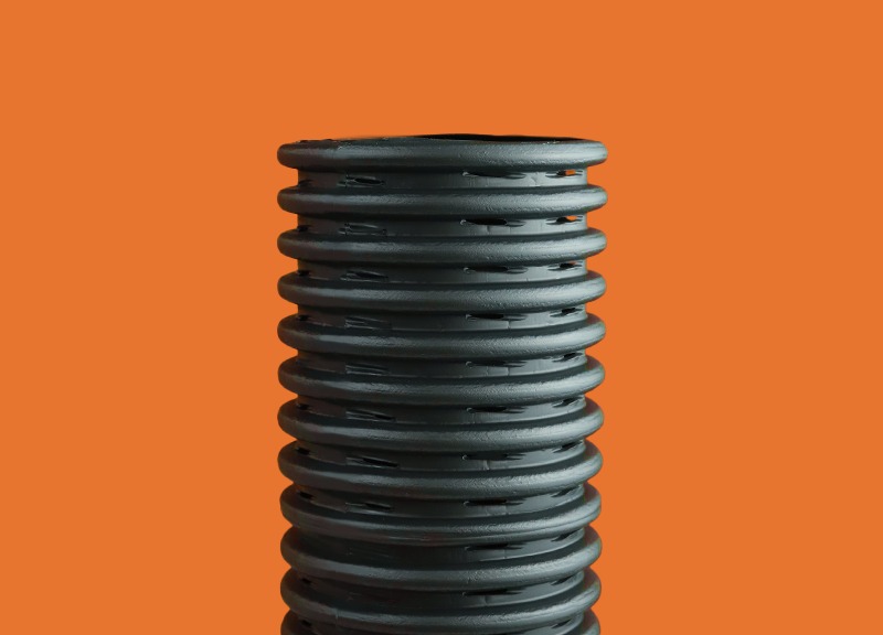 Tucano Dreno, tubulação corrugada preta, com pequenos furos para saída de água evidenciando sua aplicação em sistemas de drenagem, contra um fundo laranja que destaca a peça.